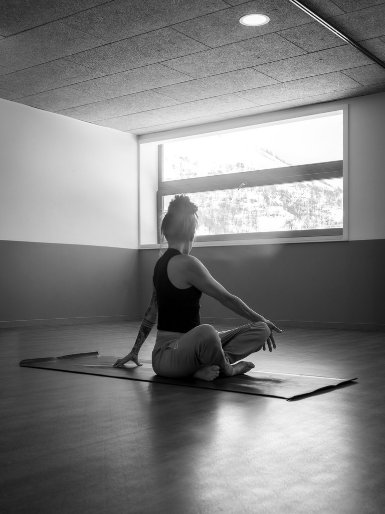 Cécilia assise en tailleur, tournée vers la fenêtre, dans une posture de Yoga.